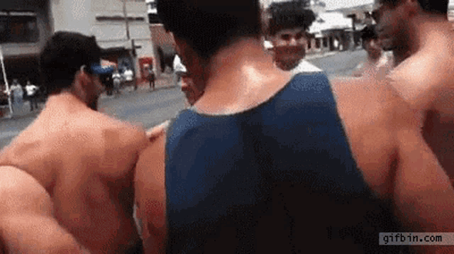 a group of shirtless men are standing on a street with a gifbin.com logo in the corner .