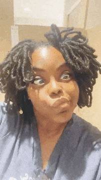 a woman with dreadlocks is making a funny face while looking at the camera .