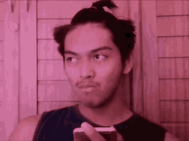a man with a ponytail is holding a cell phone and making a funny face