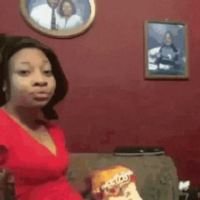 a woman in a red dress is sitting on a couch eating cheetos