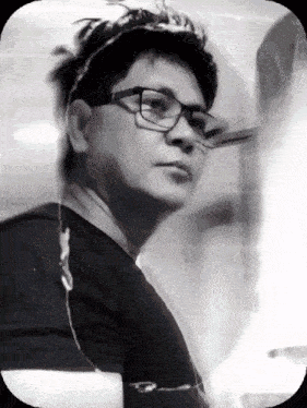 a man with glasses and a black shirt looks at the camera