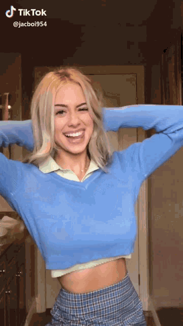 a woman is wearing a blue sweater and a plaid skirt and has a tiktok on her phone