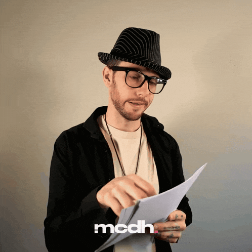 a man wearing a hat and glasses is holding a piece of paper with the letters mcdh on the bottom