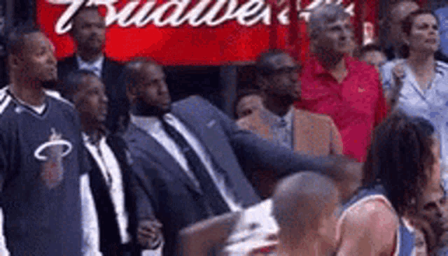 a group of men are standing in front of a budweiser sign watching a basketball game .