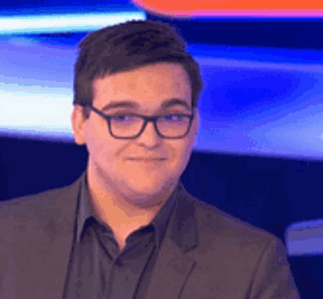 a man wearing glasses and a suit is smiling while standing in front of a blue background .