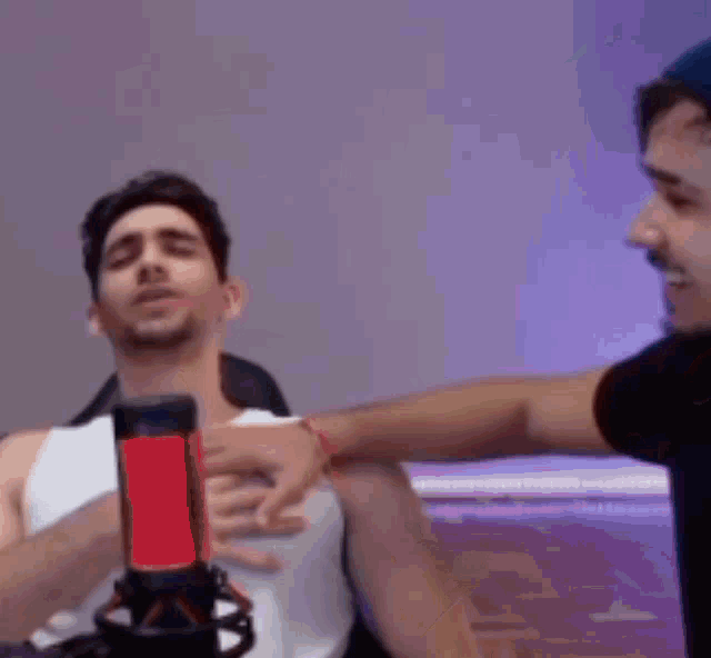 a man is tickling another man in front of a microphone while laying on a bed .