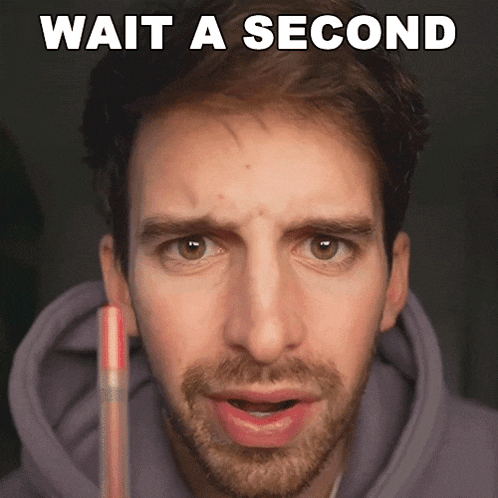 a man is holding a pencil in front of his face and the words wait a second are above him