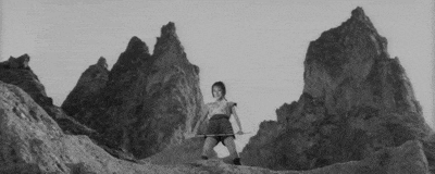 a black and white photo of a woman standing on top of a mountain holding a sword .