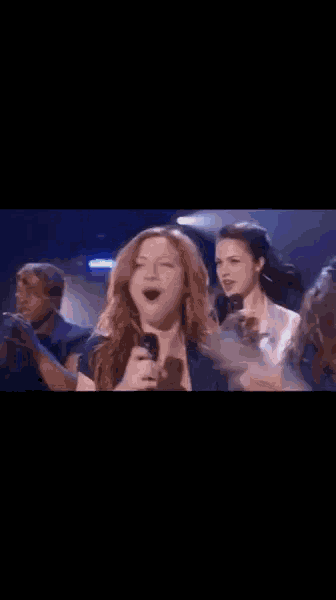 a woman is singing into a microphone while a group of people point at her