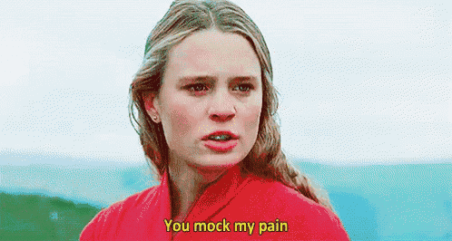 a woman in a red shirt is standing in front of a body of water and saying `` you mock my pain '' .