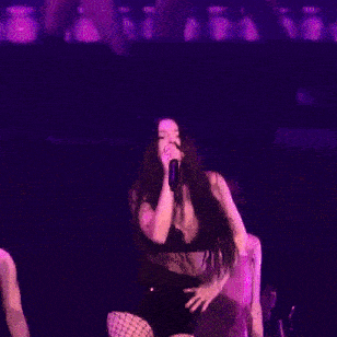 a woman is singing into a microphone on a stage in a purple light .
