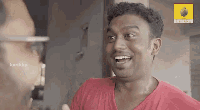 a man in a red shirt is laughing and talking to another man in a room .