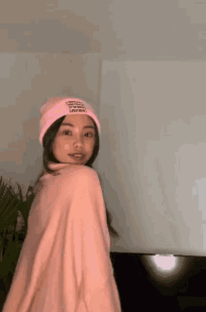 a woman wearing a pink beanie and a pink sweater is standing in front of a wall .