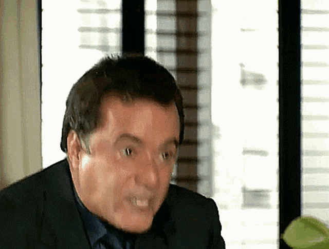 a man in a suit and tie is making a funny face in front of a window