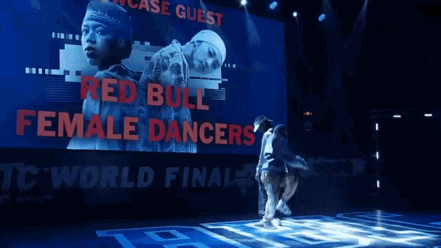 red bull female dancers perform on a stage in front of a large screen