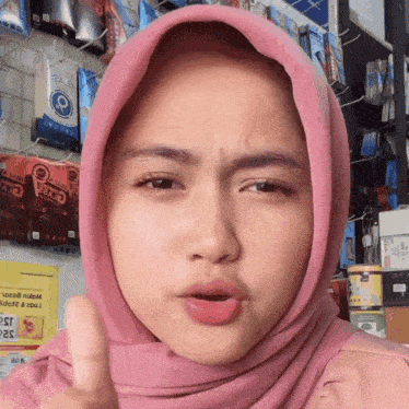 a woman wearing a pink hijab gives a thumbs up sign
