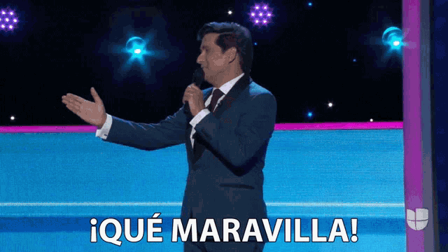 a man in a suit and tie holds a microphone and says iqué maravilla