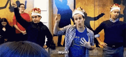 a group of men wearing crowns are dancing in a room and one of them is saying `` work '' .