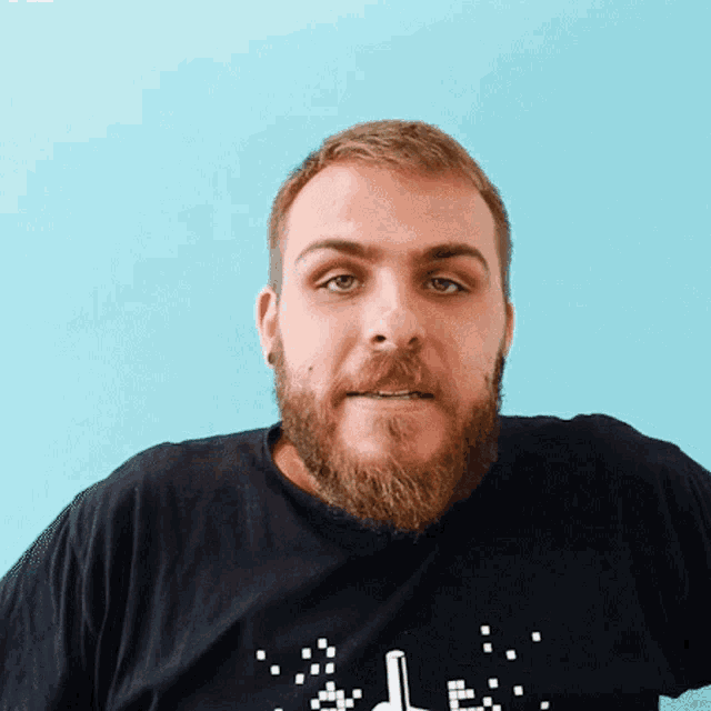 a man with a beard is wearing a black t-shirt with a pixelated hand pointing to the left