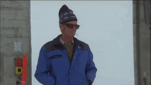 a man in a blue jacket smoking a cigarette and wearing sunglasses