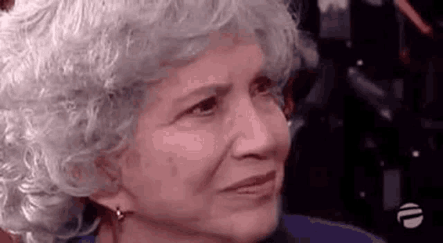 a close up of an older woman with gray hair and earrings making a funny face .