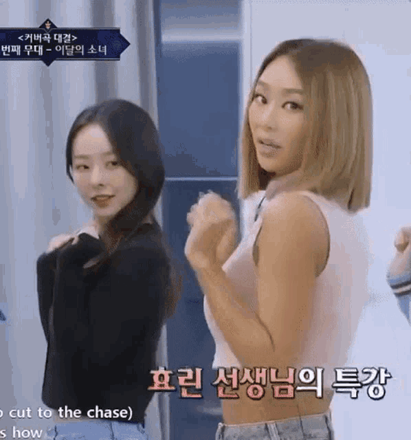 two women are standing next to each other and one of them is wearing a pink tank top and a black sweater .