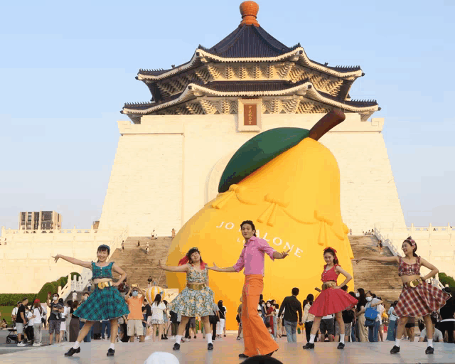 a group of people are dancing in front of a giant pear that says jo malone