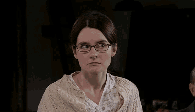 a woman wearing glasses and a white shirt looks down