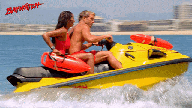 a man and a woman are riding a yellow jet ski with baywatch written in red