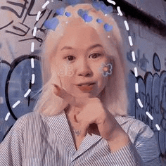 a woman with blonde hair and a flower in her hair is standing in front of a graffiti wall .