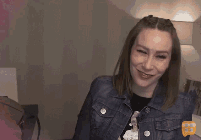 a woman wearing a denim jacket winks at the camera with the number 8 visible in the corner