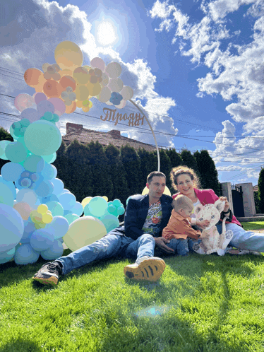 a family sits on the grass in front of balloons and a sign that says " mpogii " on it