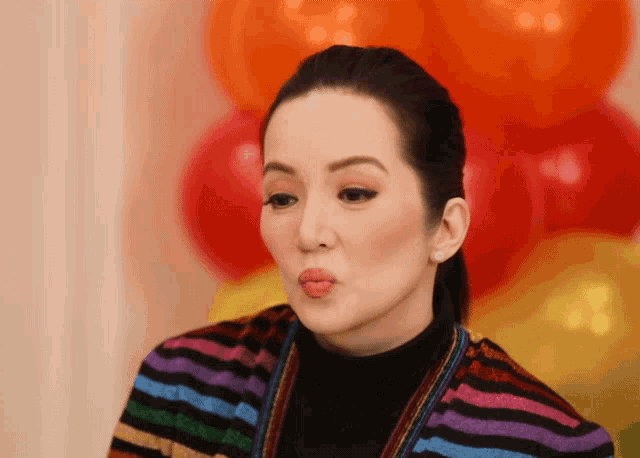 a woman wearing a striped sweater is blowing a kiss in front of balloons