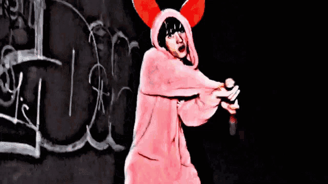 a girl in a pink bunny costume is standing in front of a black wall with graffiti on it