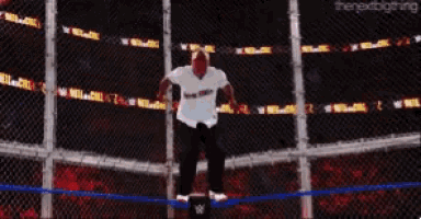 a man in a white shirt stands in a wrestling ring behind a chain link fence ..