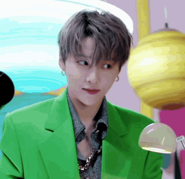 a young man wearing a green jacket and earrings is looking at the camera .