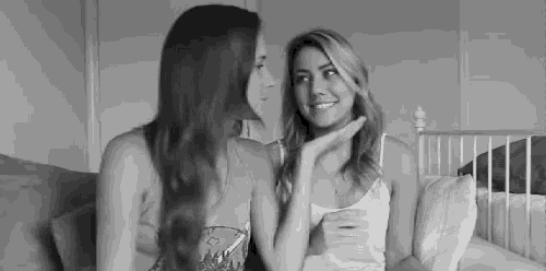 two women are sitting next to each other on a bed talking to each other .
