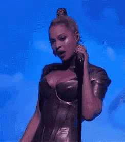 a woman in a leather dress is singing into a microphone on stage .