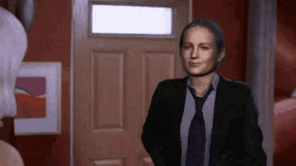 a woman in a suit and tie is standing in front of a wooden door