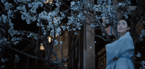 a woman in a blue dress stands under a tree with white flowers