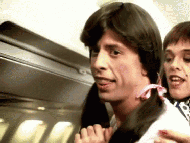 a man wearing a wig and pigtails is talking to a woman on an airplane .