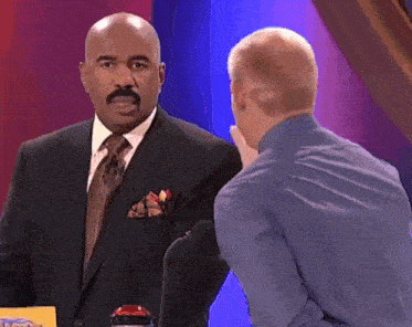 a man in a suit and tie talking to another man in a blue shirt