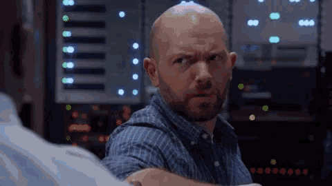 a bald man with a beard is making a funny face in front of a server room .