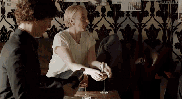 a man is pouring a glass of wine into a woman 's glass while they sit at a table