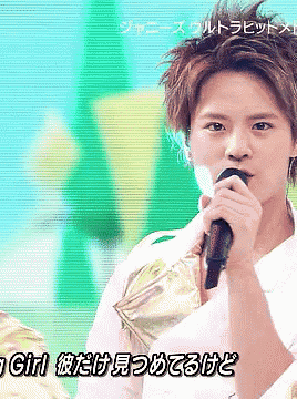 a young man singing into a microphone with foreign writing on the bottom right
