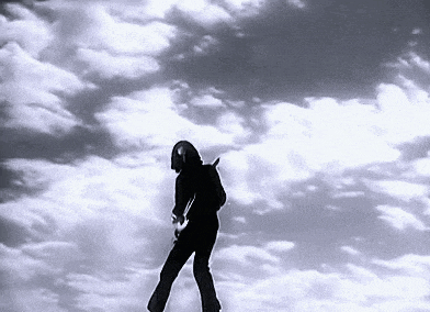 a black and white photo of a person playing a guitar against a cloudy sky