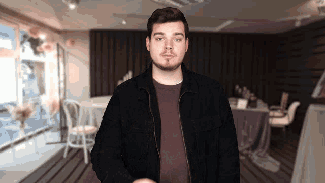 a man in a black jacket stands in front of a table and chairs