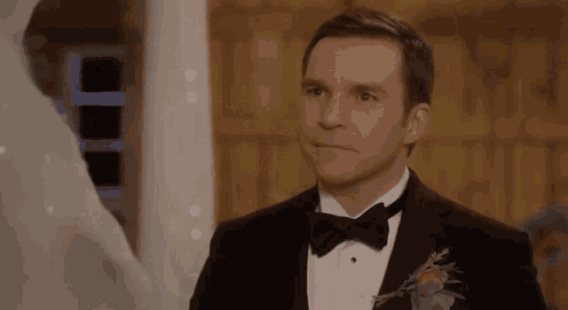 a man in a tuxedo and bow tie is standing next to a woman in a wedding dress .