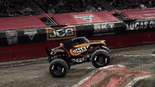 a monster truck is driving on a dirt track with a jcb banner behind it