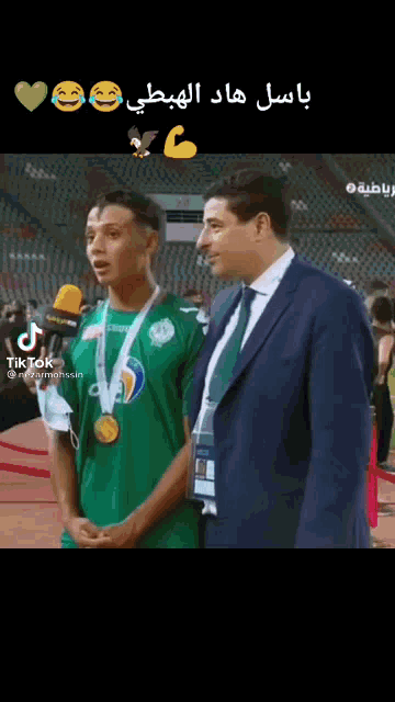 a man in a suit is standing next to a man in a green shirt with a medal around his neck